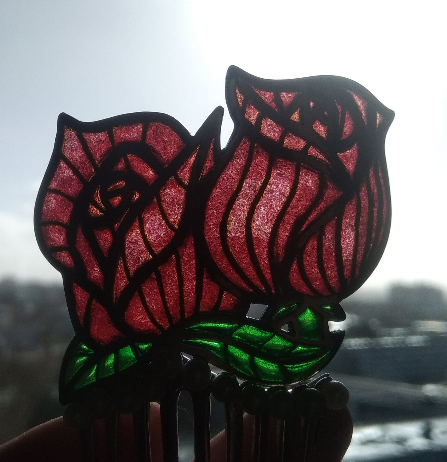 Photographie de l'effet de transparence de la technique de l'émail plique à jour sur un peigne en argent représentant deux roses émaillées en rouge et vert.